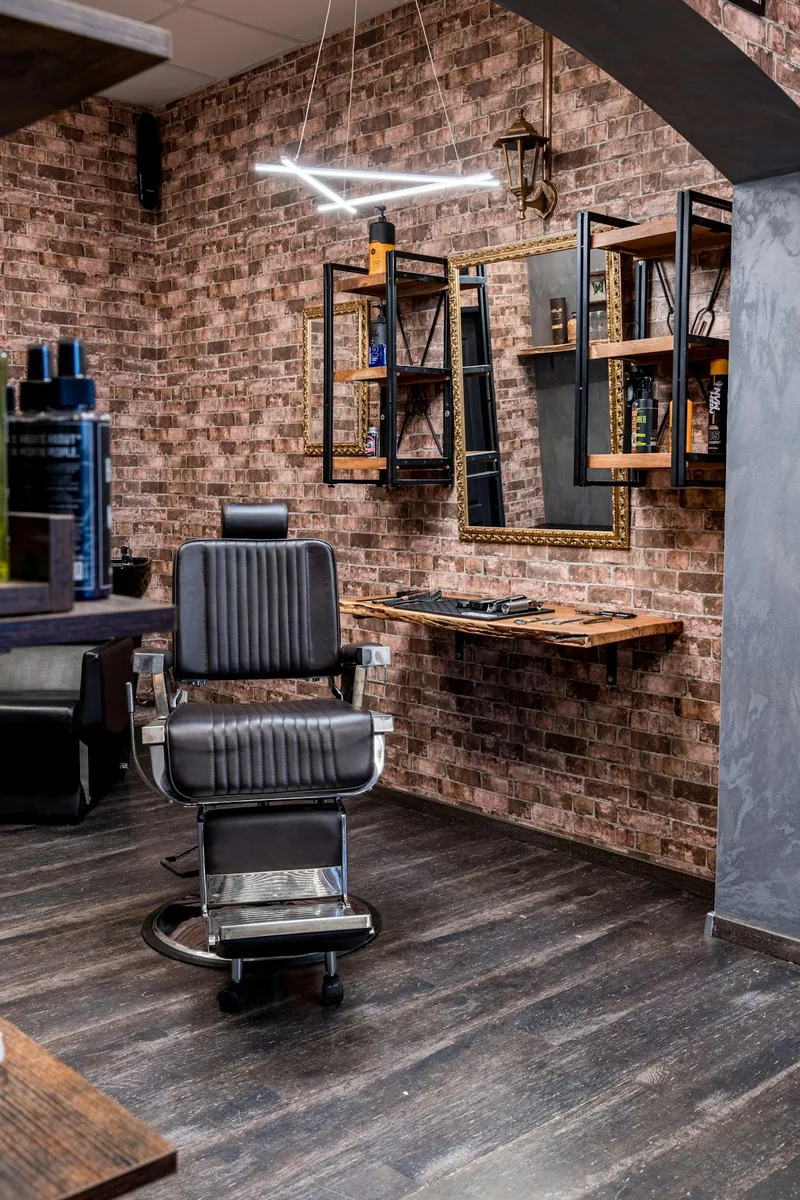 Rincón de la barbería con sillón negro, pared de ladrillo y espejo con marco dorado