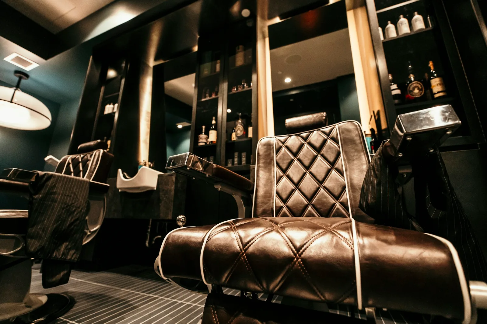 Interior de una barbería oscura y moderna, con sillones de cuero y un espejo iluminado